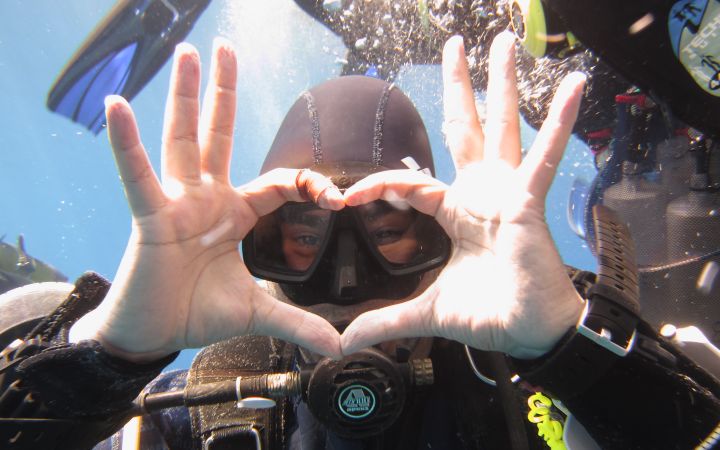Underwater photo of Dr. Sameh Al-Muqdadi in diving gear, showing heart-shaped hands
