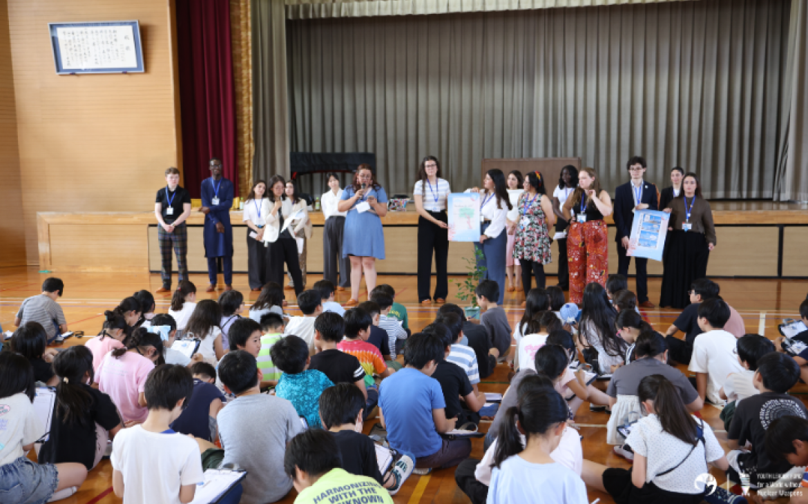 YLF participants standing in front of a room in front of elementary students, sitting and listening to their stories