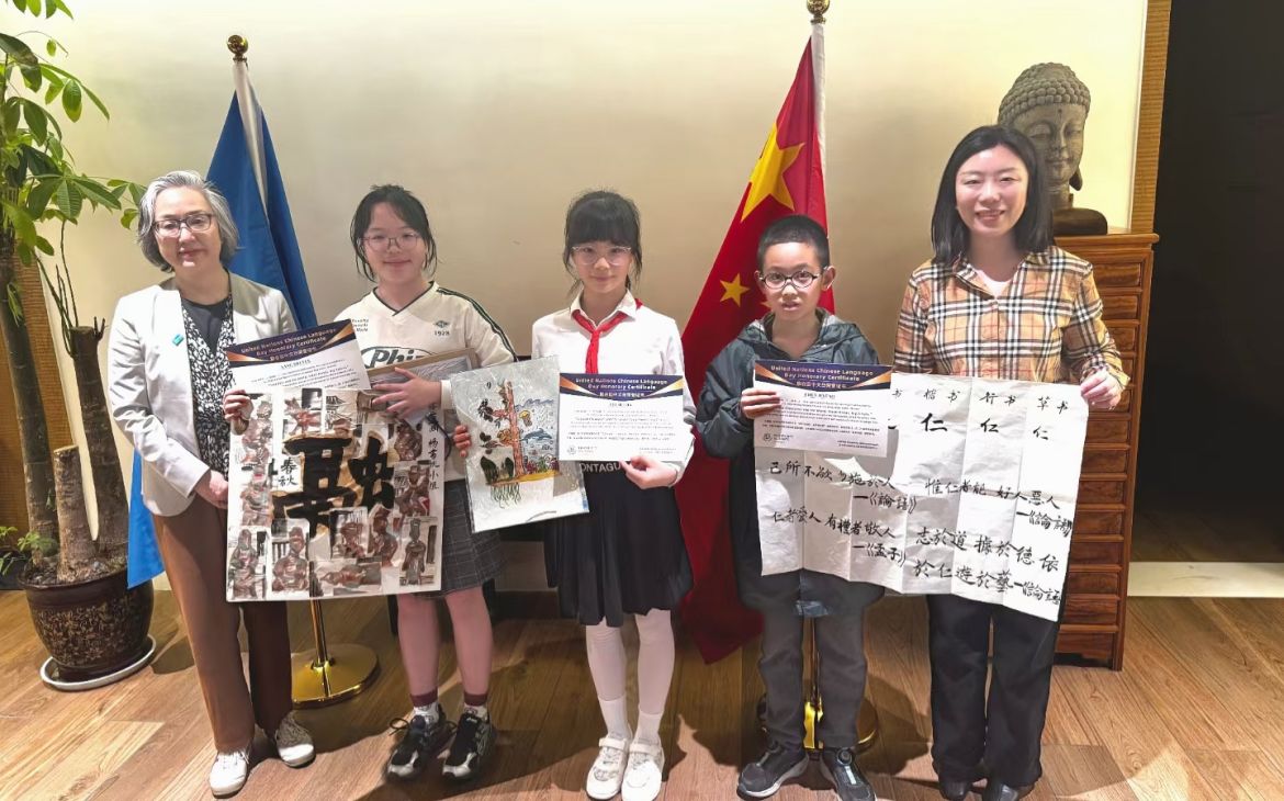 An older professional stands with four children who hold up their artwork.