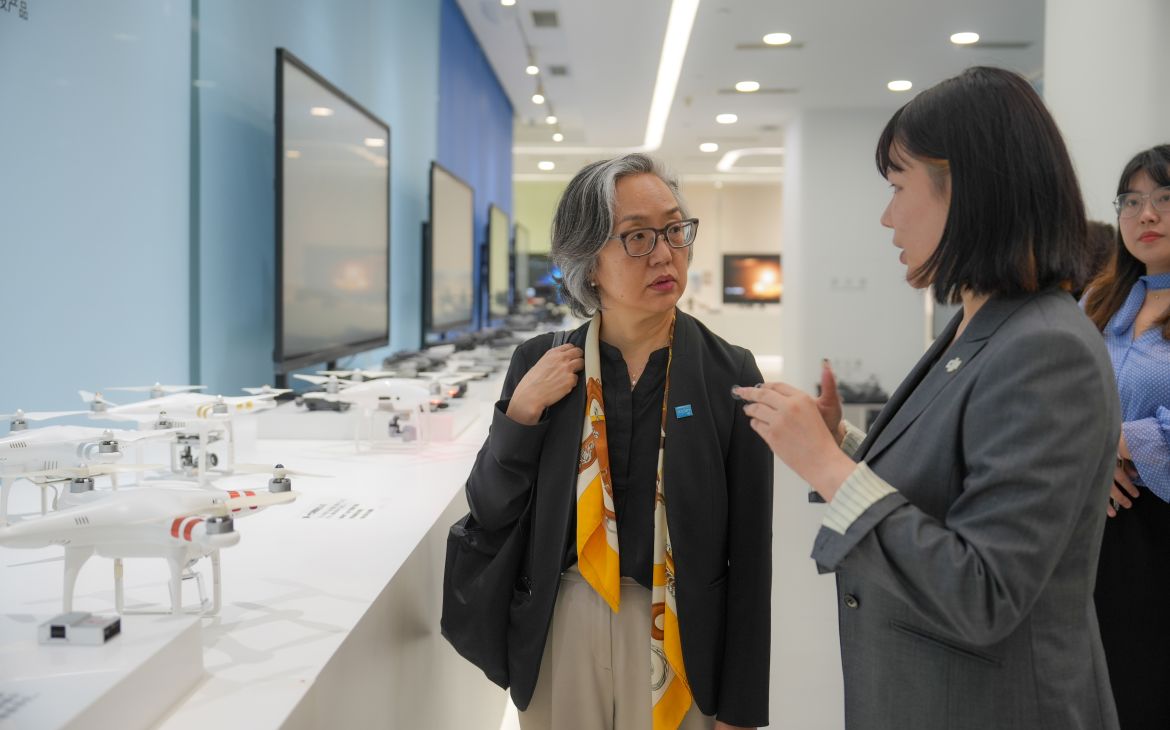 East Asian woman with short grey hair listens carefully as younger Asian woman explains the drones on display.