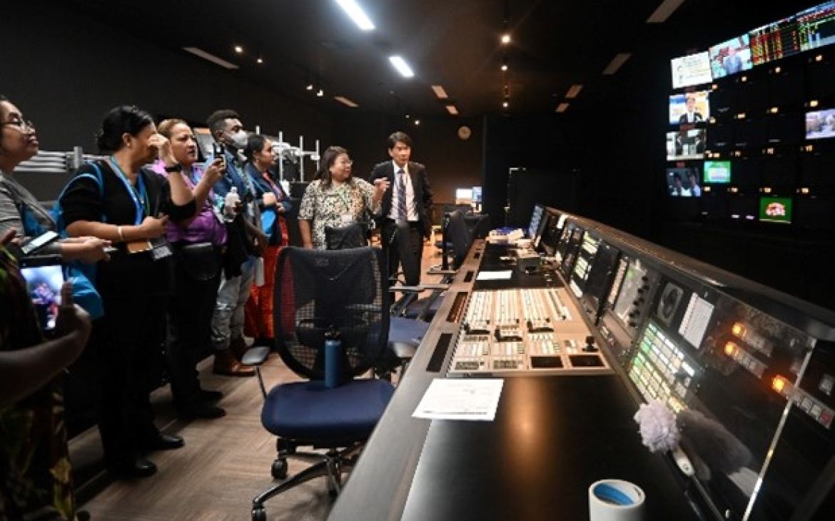 A group of Pacific Islanders observe a large console with multiple screens.