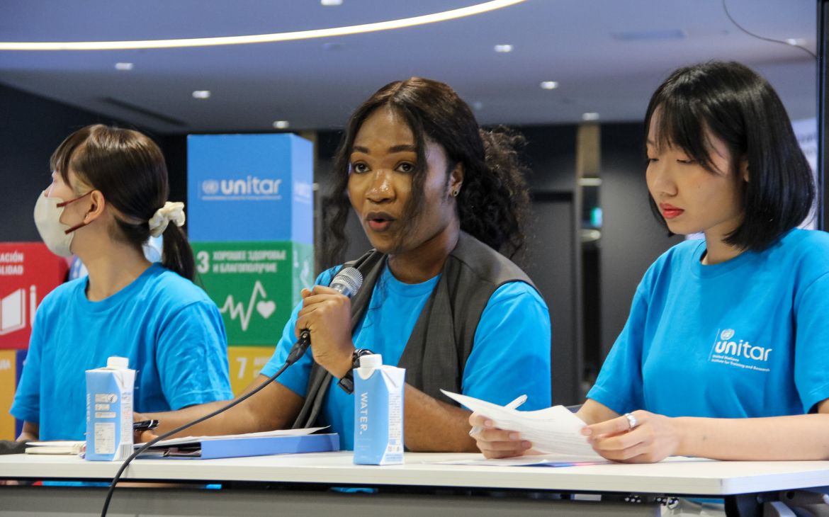 Three young participants sitting behind a long table and the person in the middle speaking through a microphone