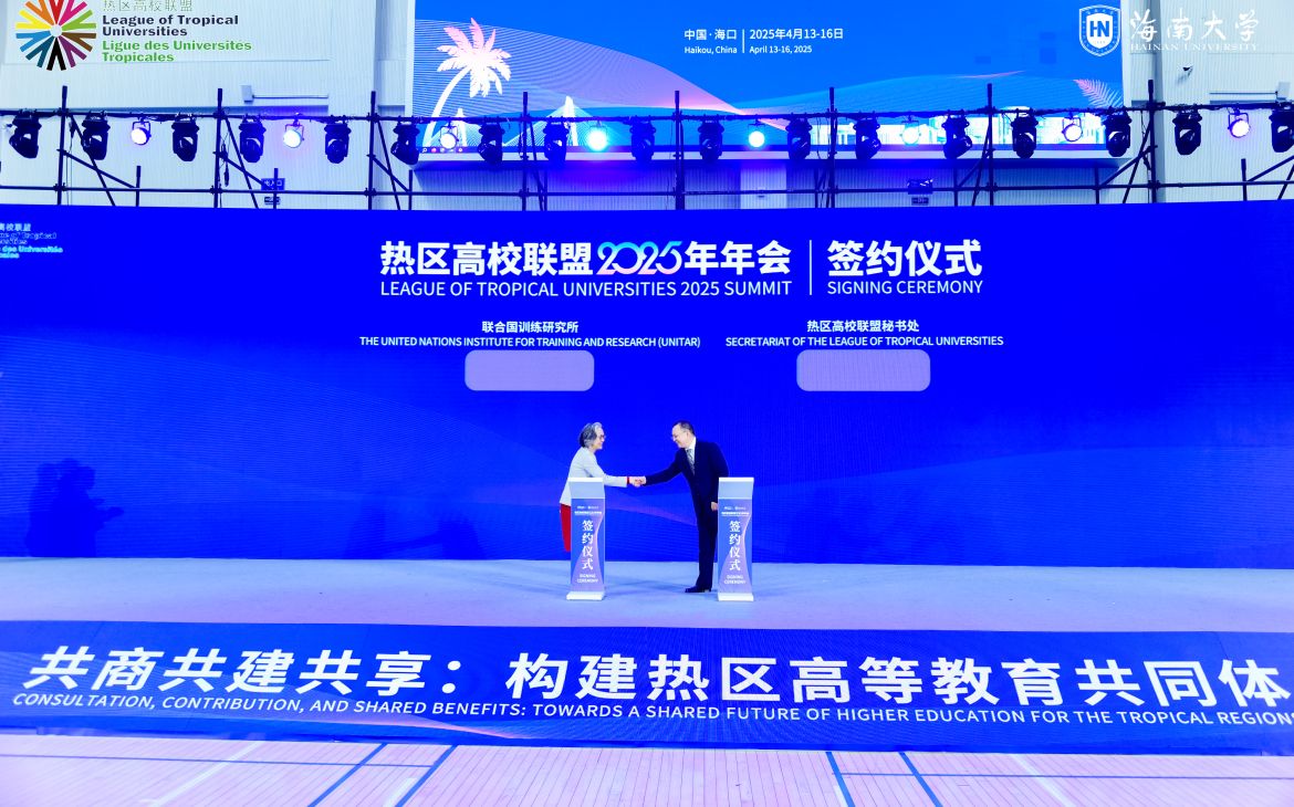 An East Asian woman and man shake hands in the middle of a huge, blue stage.