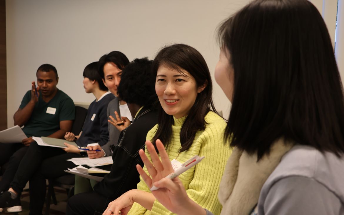 A participant speaking to a person next to her in a room and other participants are also in the background