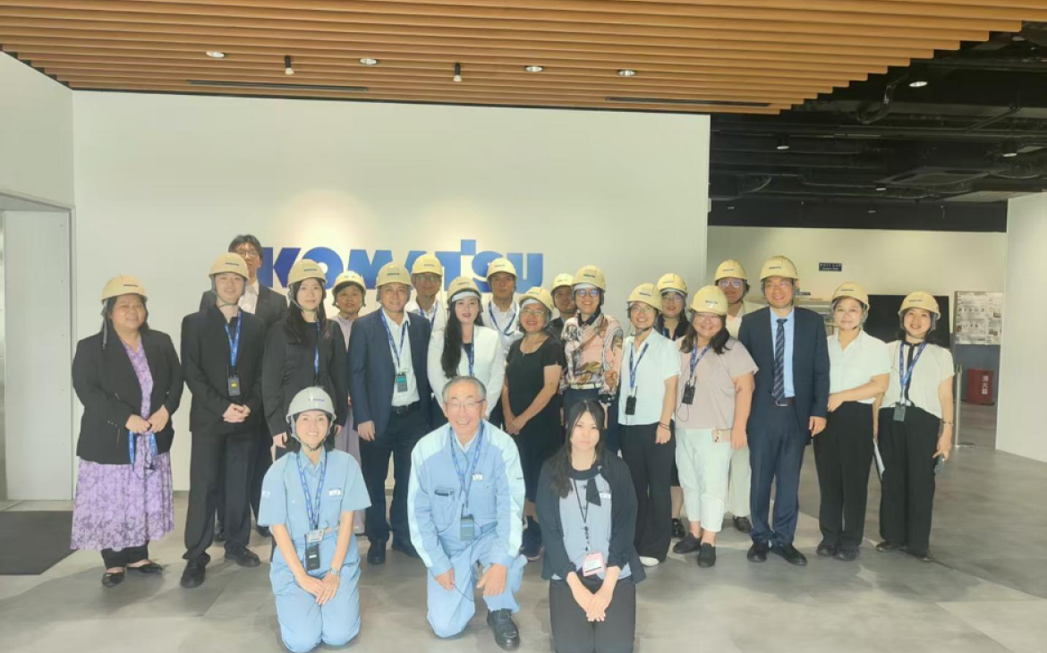A group photo in front of the Komatsu Ltd. Logo