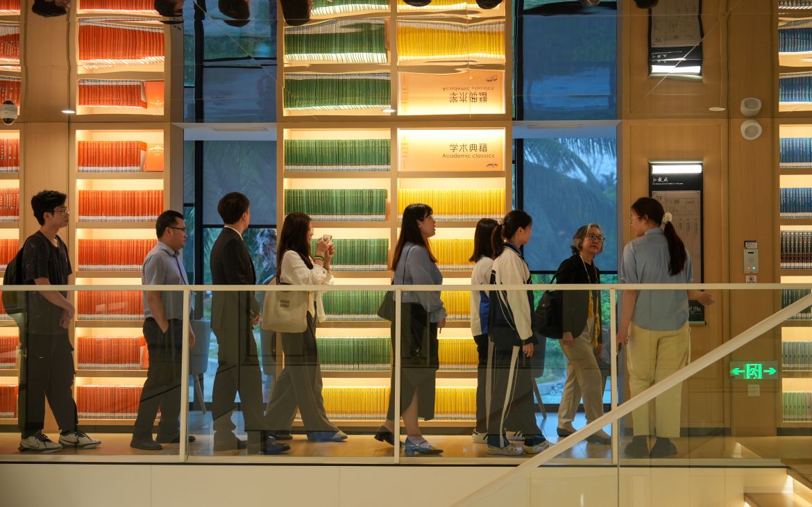 Group of East Asian men and women walk along colourful wall lined with bookshelves.