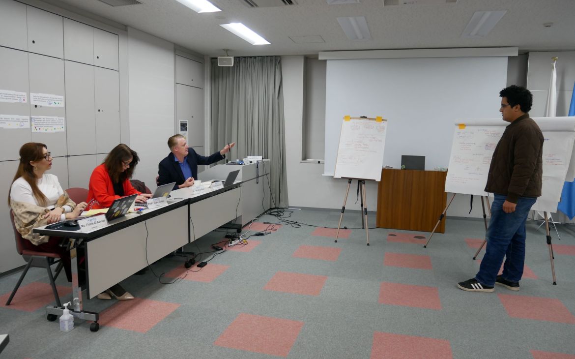 A person presenting in front of three experts sitting across from the presenter.