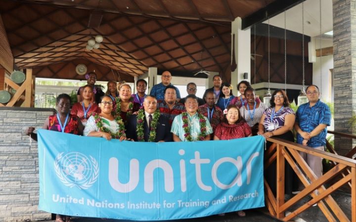 A group of participants from the Pacific stand in front of a UNITAR banner for a group photo