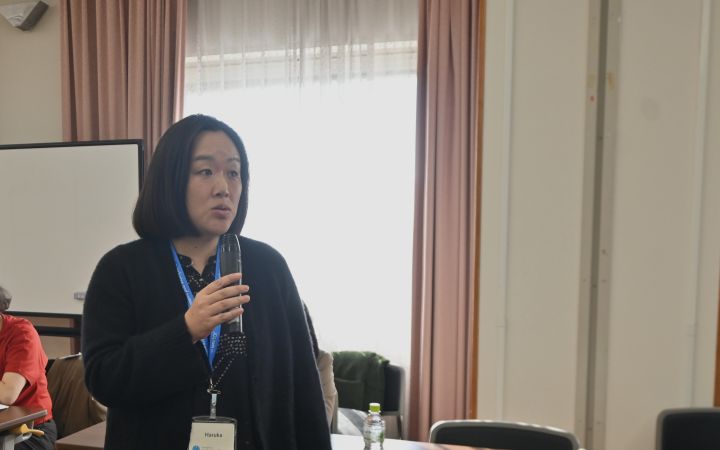 A person speaking through a microphone in a room to other participants