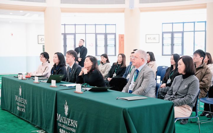 Business professional women and men sit in a long conference table.