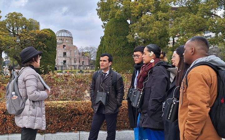 Six participants from the UNITAR Nuclear Disarmament Programme receiving a lecture from a Japnese lady near the Hiroshima A bomb dome