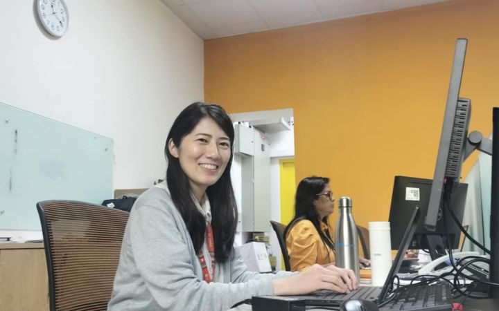 A staff smiling at the camera and sitting in front of a computer