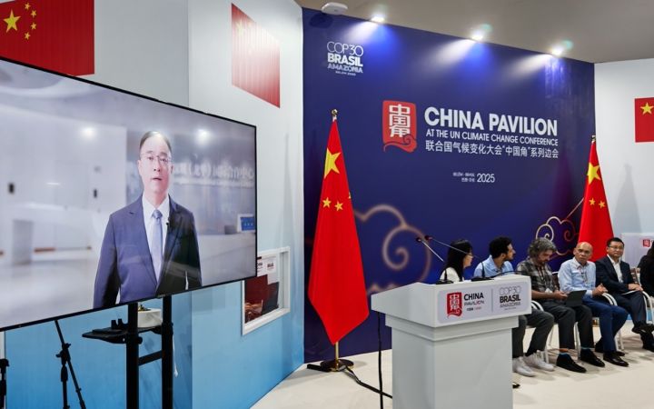 A large LED screen shows a Chinese man in a dark suit addressing the audience. To the right of the screen, a panel of six other speakers sit on the stage, with the China Pavilion backdrop and Chinese flags.
