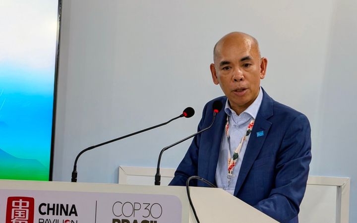 A Filipino man in a dark blue suit speaks at a podium