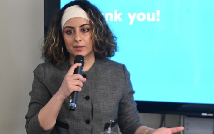 A participant standing in front of other particpants, presenting with a microphone and a screen in the background