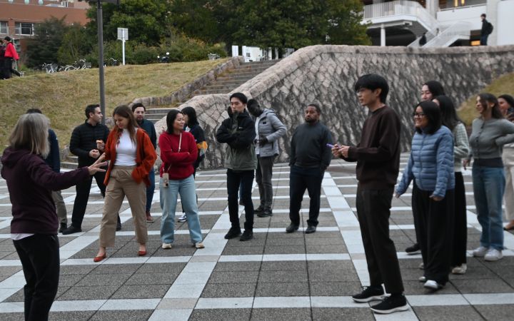 A group of participants standing and listening to a lecture outside