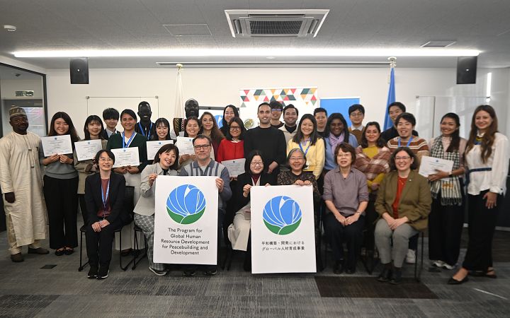 A group of program associates and staff pose in front of the camera with some holding certificates
