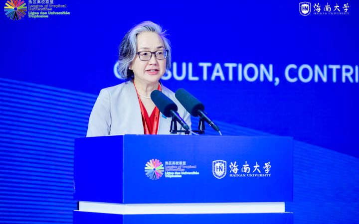 East Asian women with silver bob speaks at a podium.