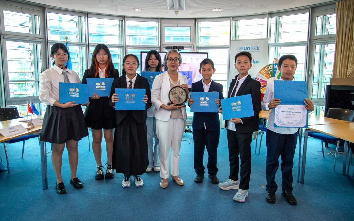 In an airy meeting room, four Chinese girls and three boys in school uniforms flank an East Asian senior professional. The students hold up their certificates for the camera.