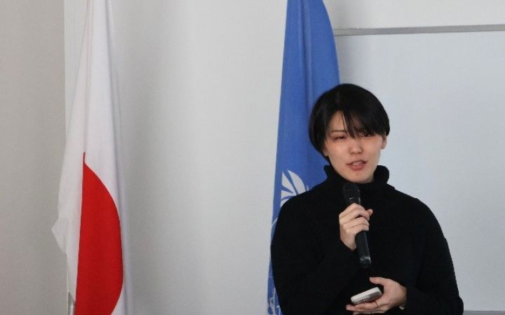 Primary Course alum from Japan speaking with a microphone in a room