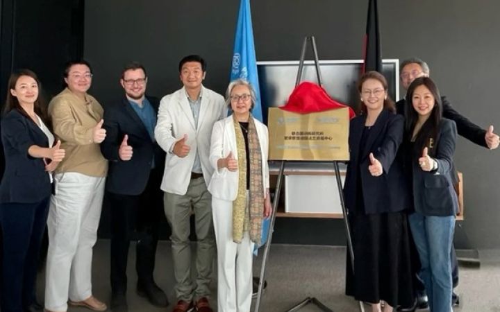 Eight smiling business women and men standing around a golden plaque and giving a thumbs up.