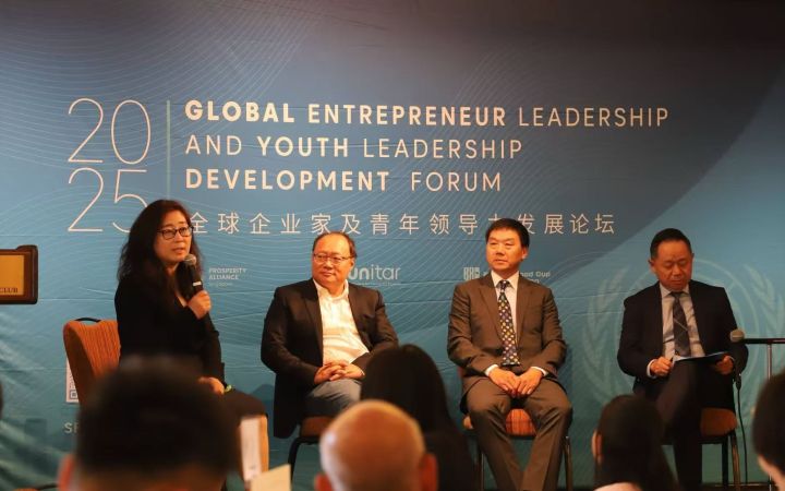 Four East Asian panellists seated in front of event backdrop. The sole woman is speaking into the microphone she holds.