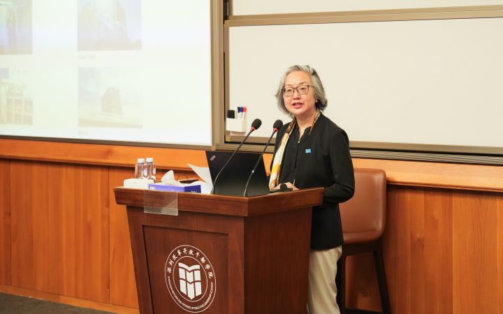 East Asian woman with grey hair speaks from a wooden podium.