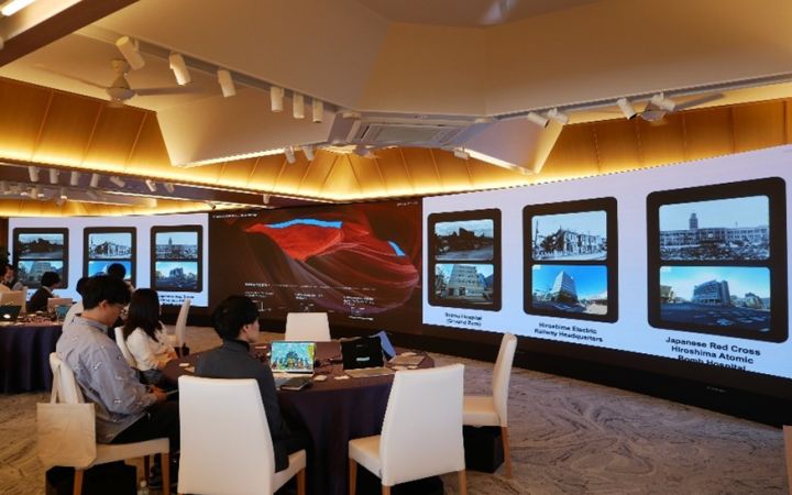 Participants sitting at a round table watching screens on the wall for a digital storytelling project presentation