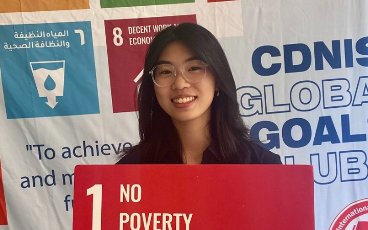 A young girl holds a cardboard sign featuring the icon and text for Sustainable Development Goal 1: "No Poverty."