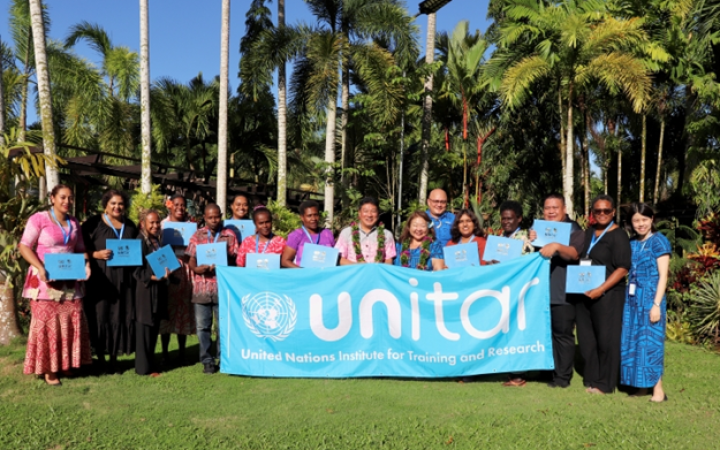 A group of participants from the Pacific standing outside with a UNITAR banner and certificate in their hands